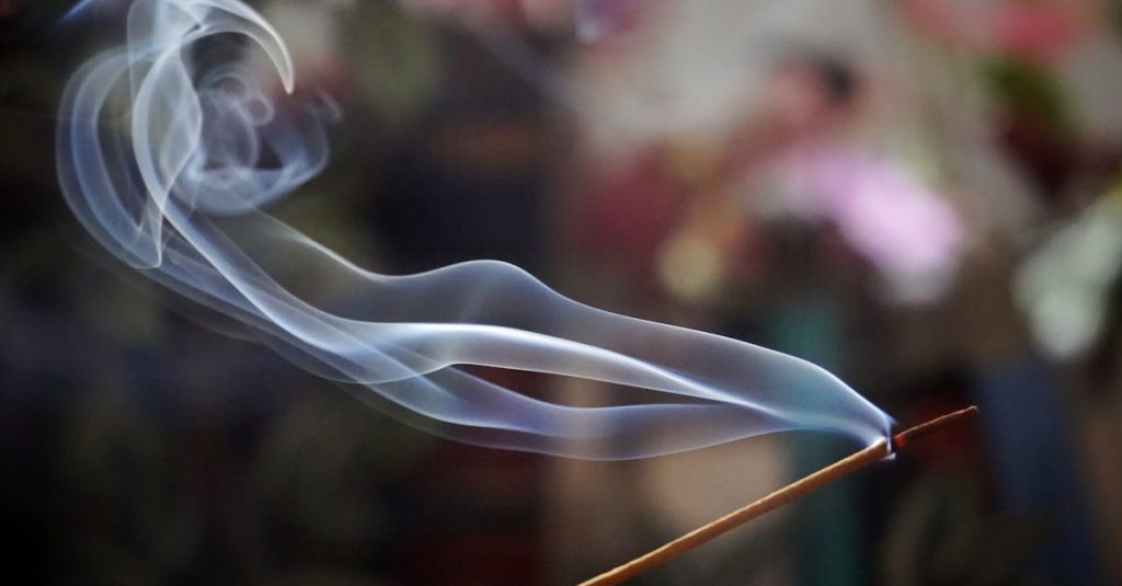 Graceful swirls of incense smoke flow softly against a colorful, blurred background.